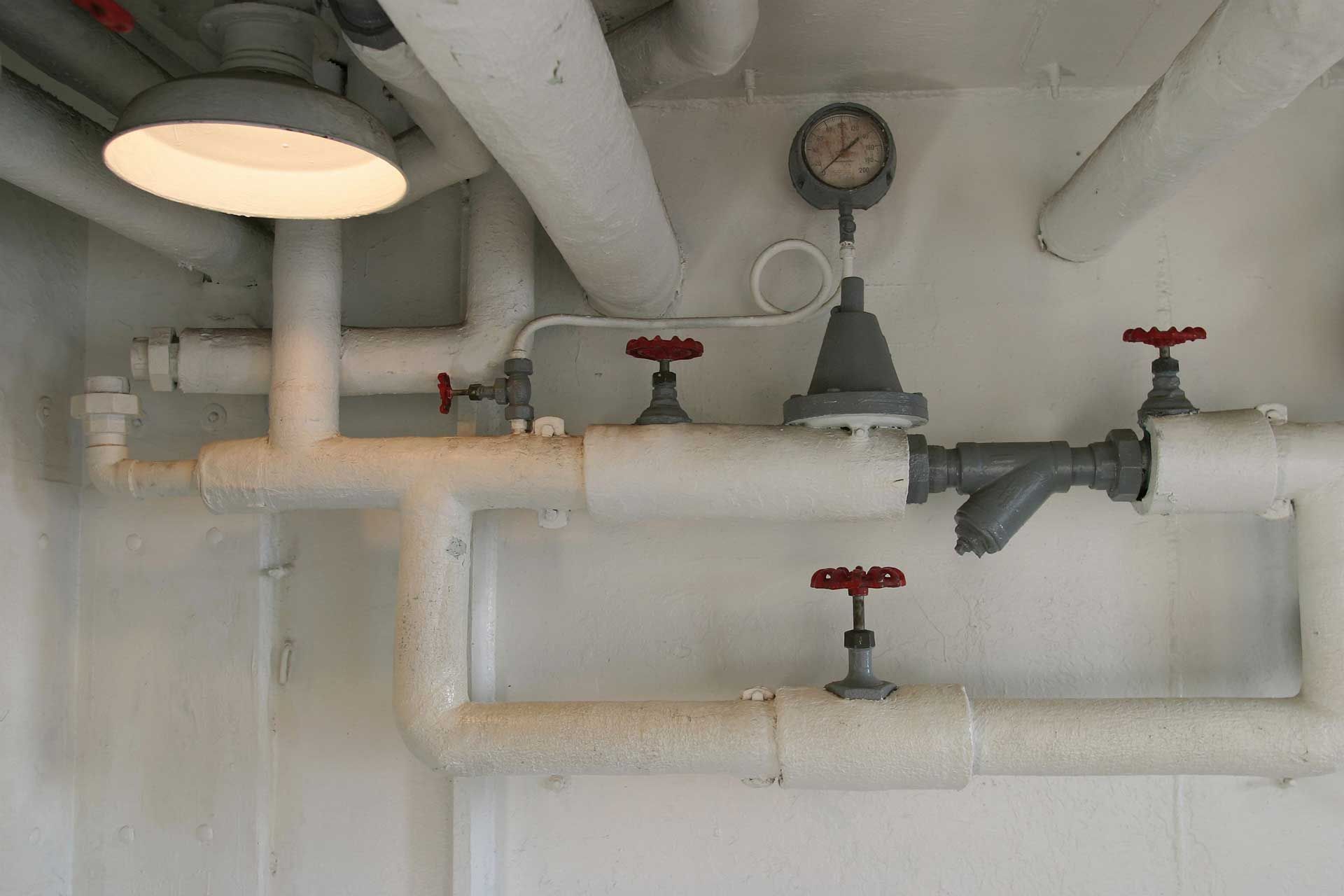 White pipes and valves with a pressure gauge and overhead light in an industrial setting.