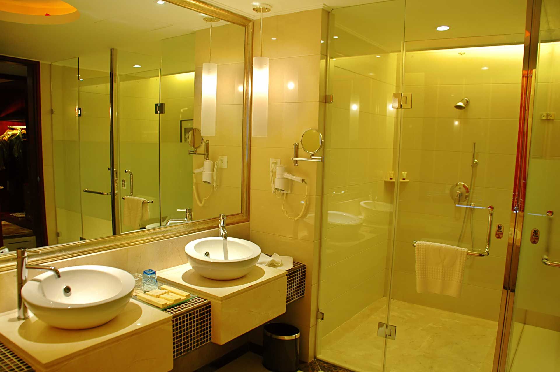 Hotel bathroom with glass shower, two sinks, and large mirror.