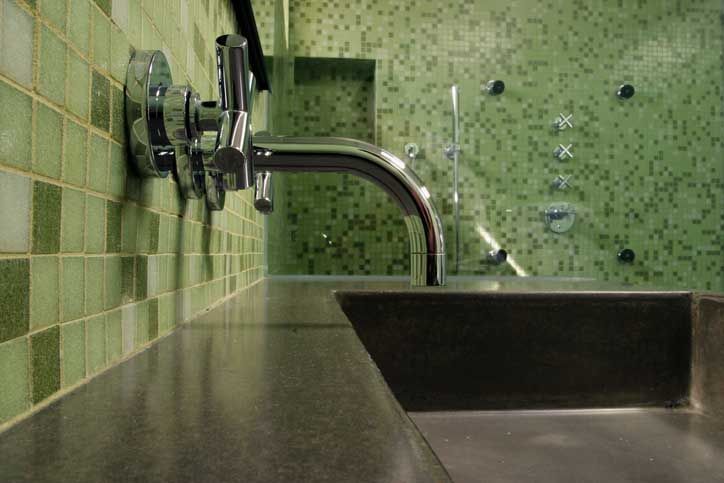 Bathroom sink with chrome faucet and green tiled walls.