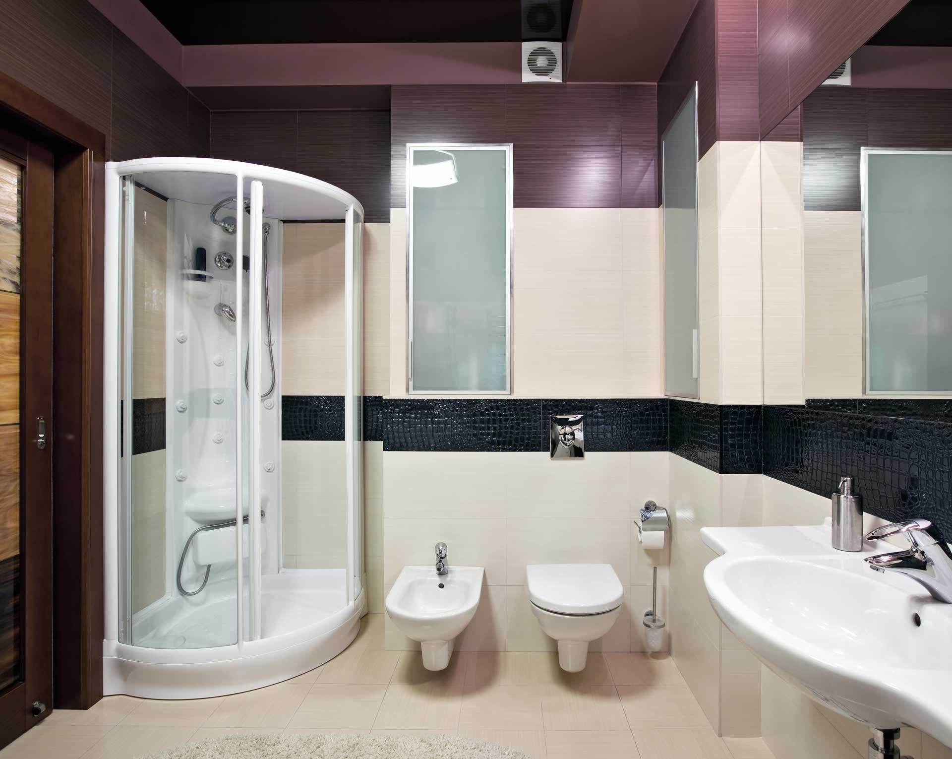 Modern bathroom with a glass shower, toilet, bidet, and sink. Beige and dark tile on the walls.