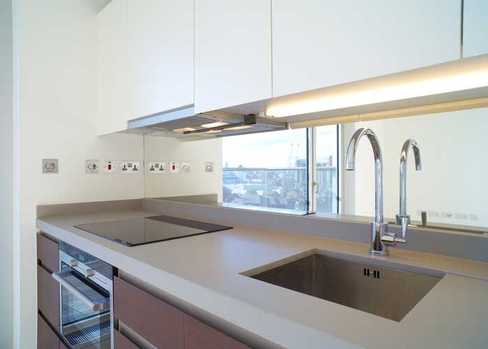 Modern kitchen with stainless steel sink and faucet, cooktop, and neutral countertops and cabinetry.