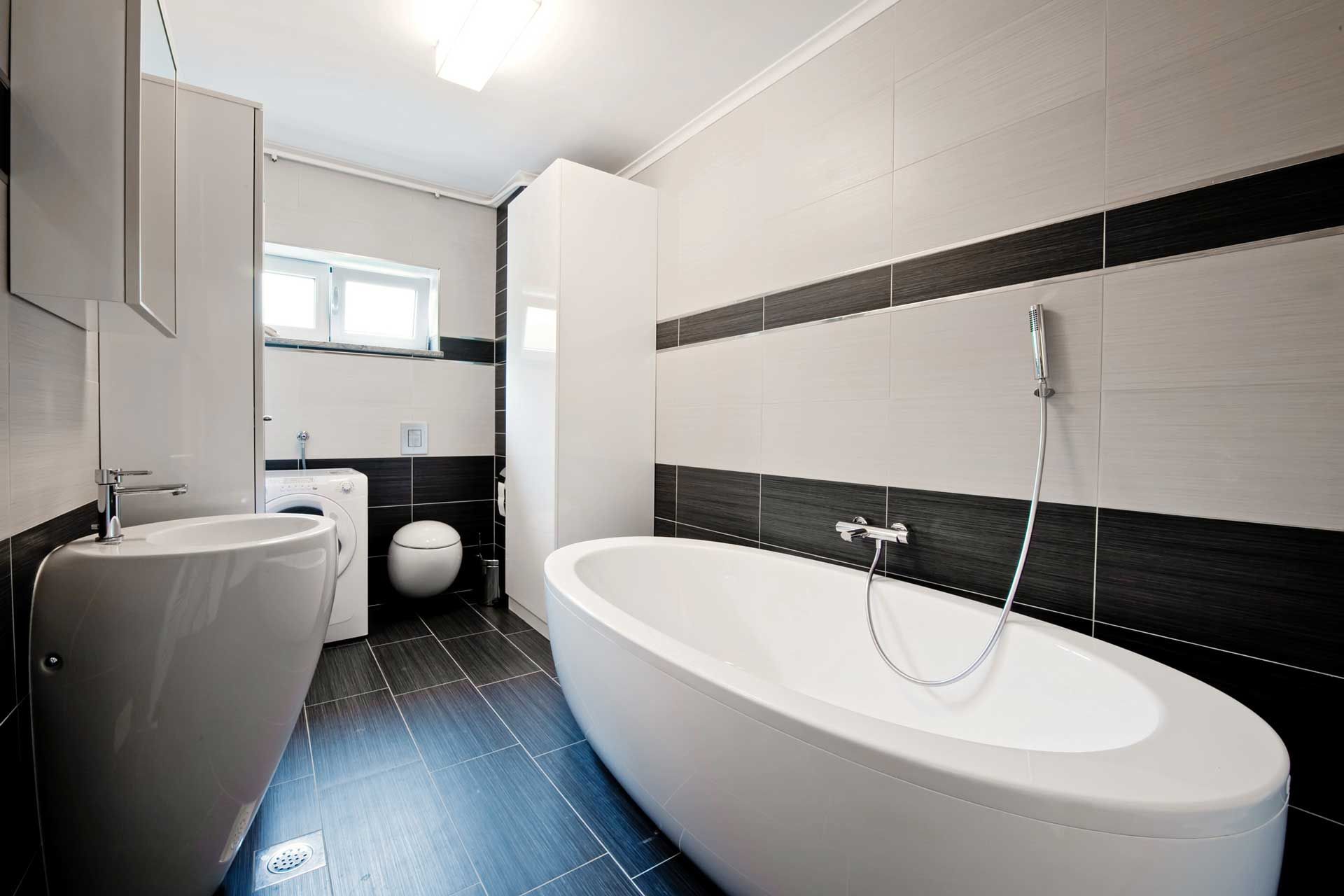 Modern bathroom with a white oval tub, sink, and toilet; black and white tile.