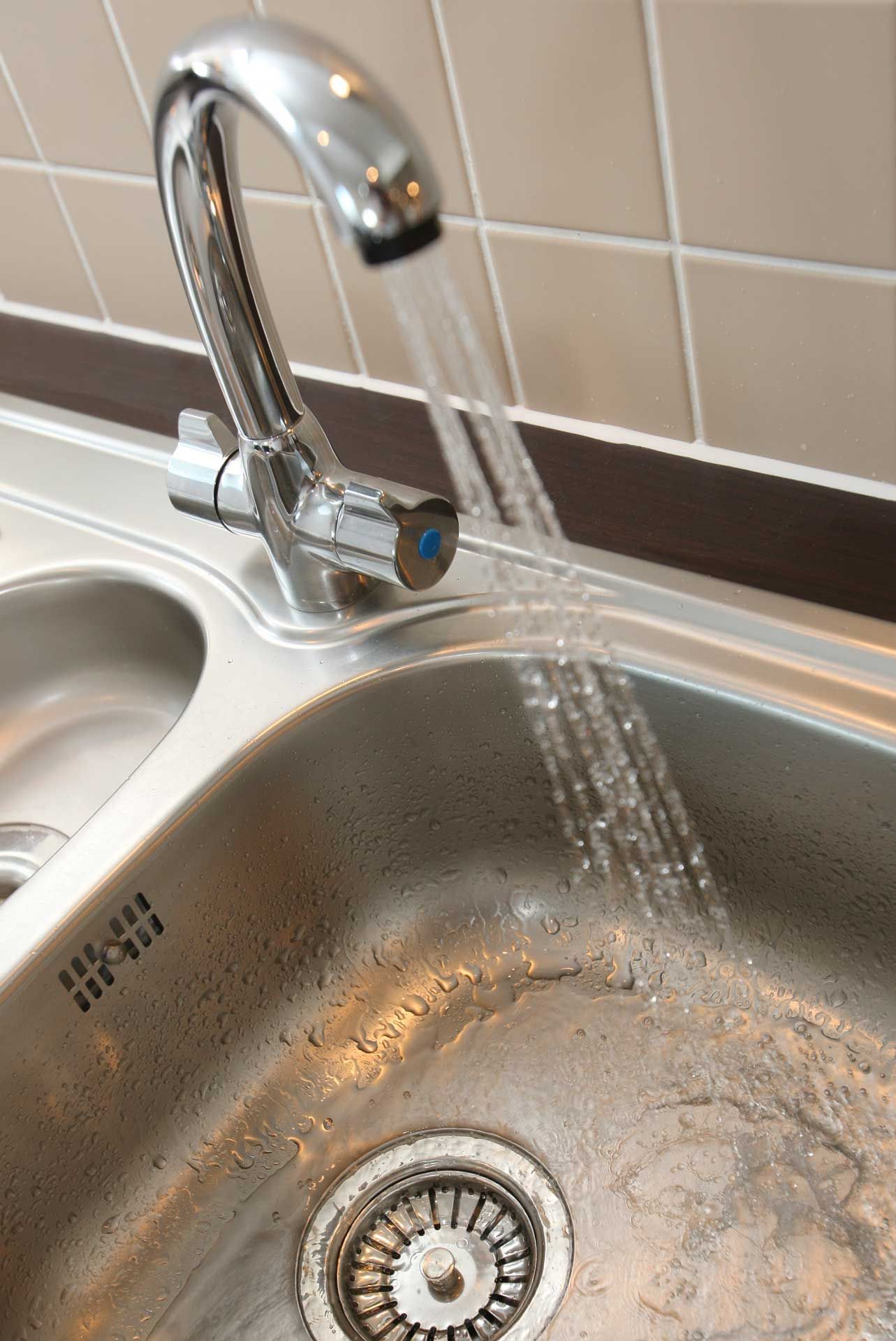 Chrome faucet with running water into a stainless steel sink.