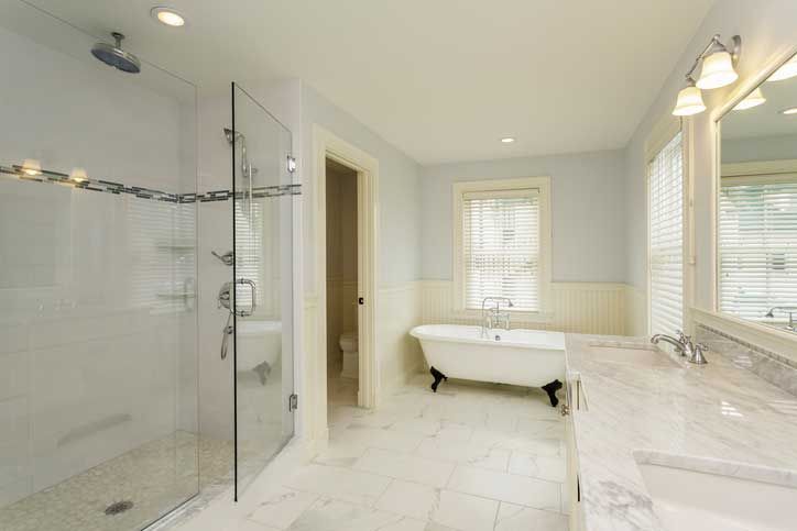 Spacious bathroom with glass shower, clawfoot tub, marble countertops, and a window with blinds.