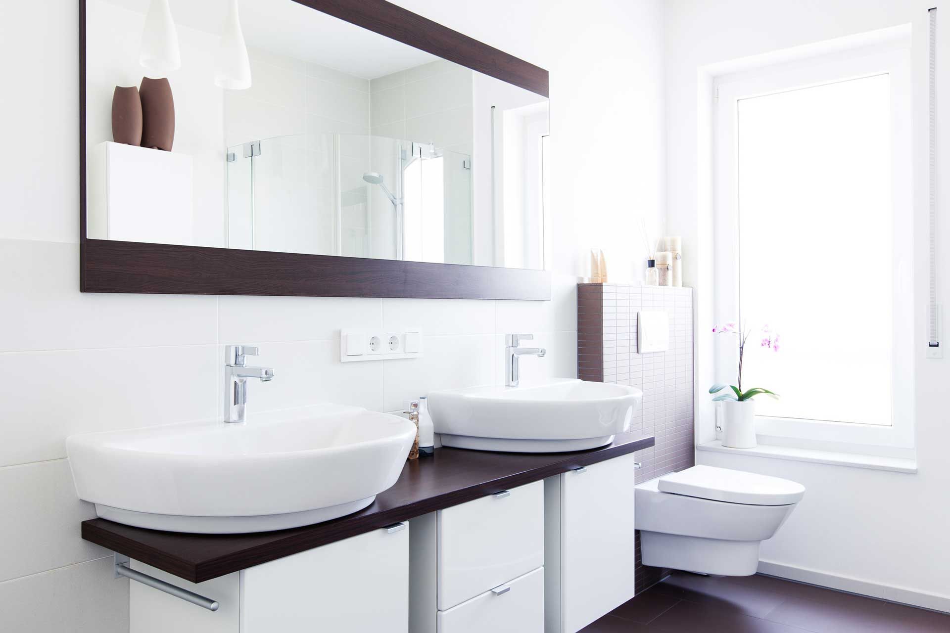 Modern white bathroom with double sinks, a large mirror, and a toilet.