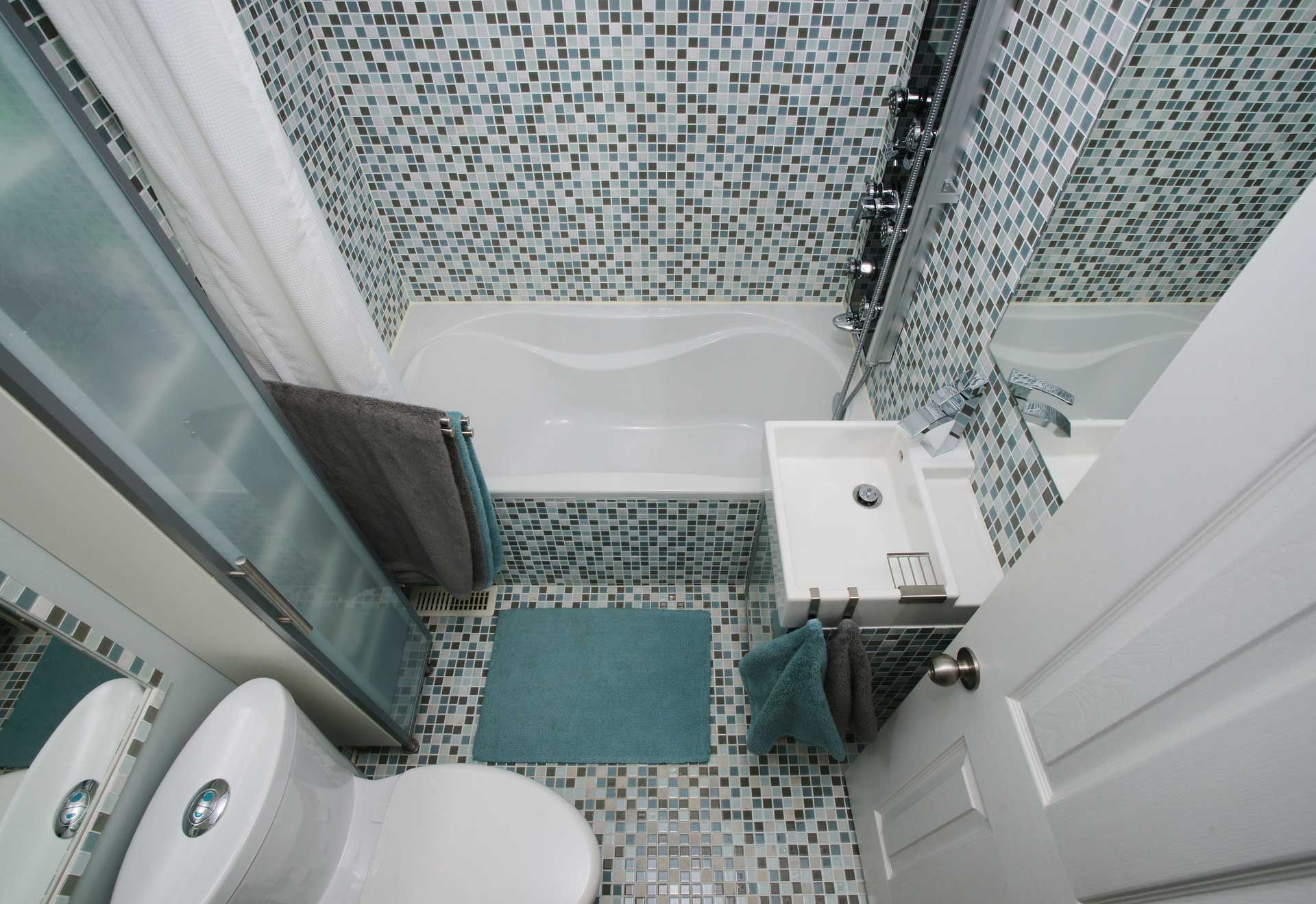 Small bathroom with mosaic tile, a bathtub, toilet, sink, and open door.