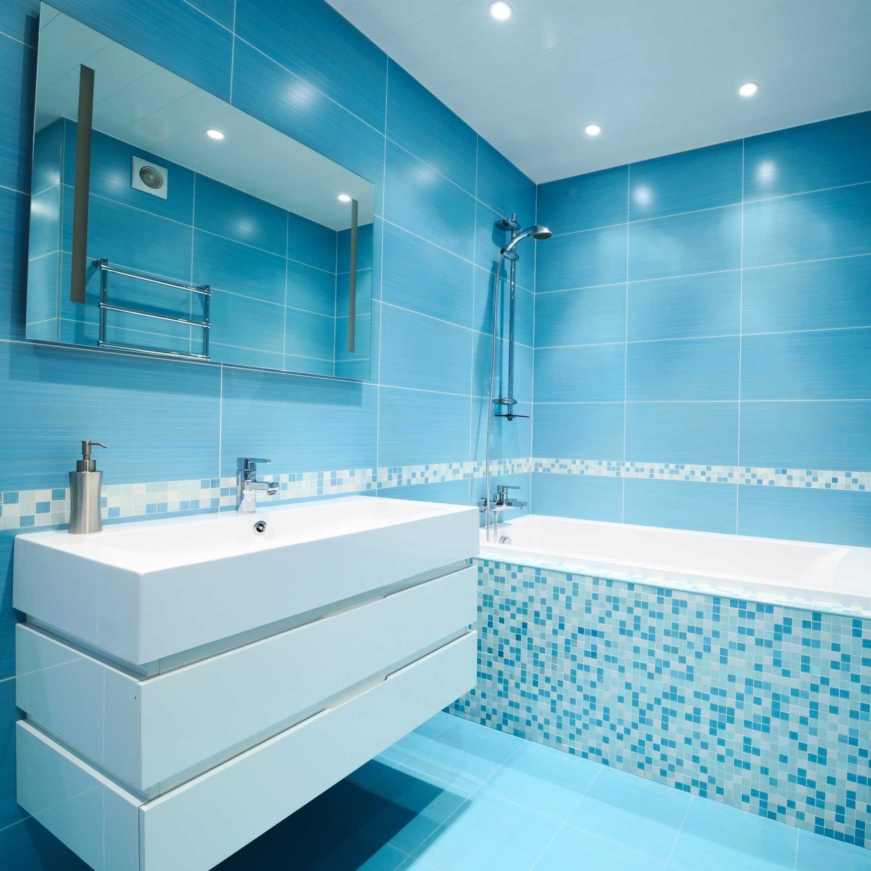 Blue-tiled bathroom with a white sink and bathtub. A large mirror hangs above the sink.