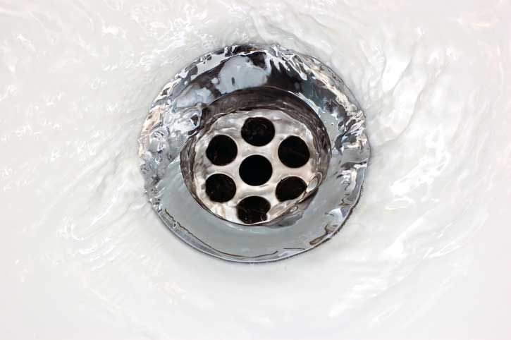 Water swirling down a shiny, round drain in a white sink.