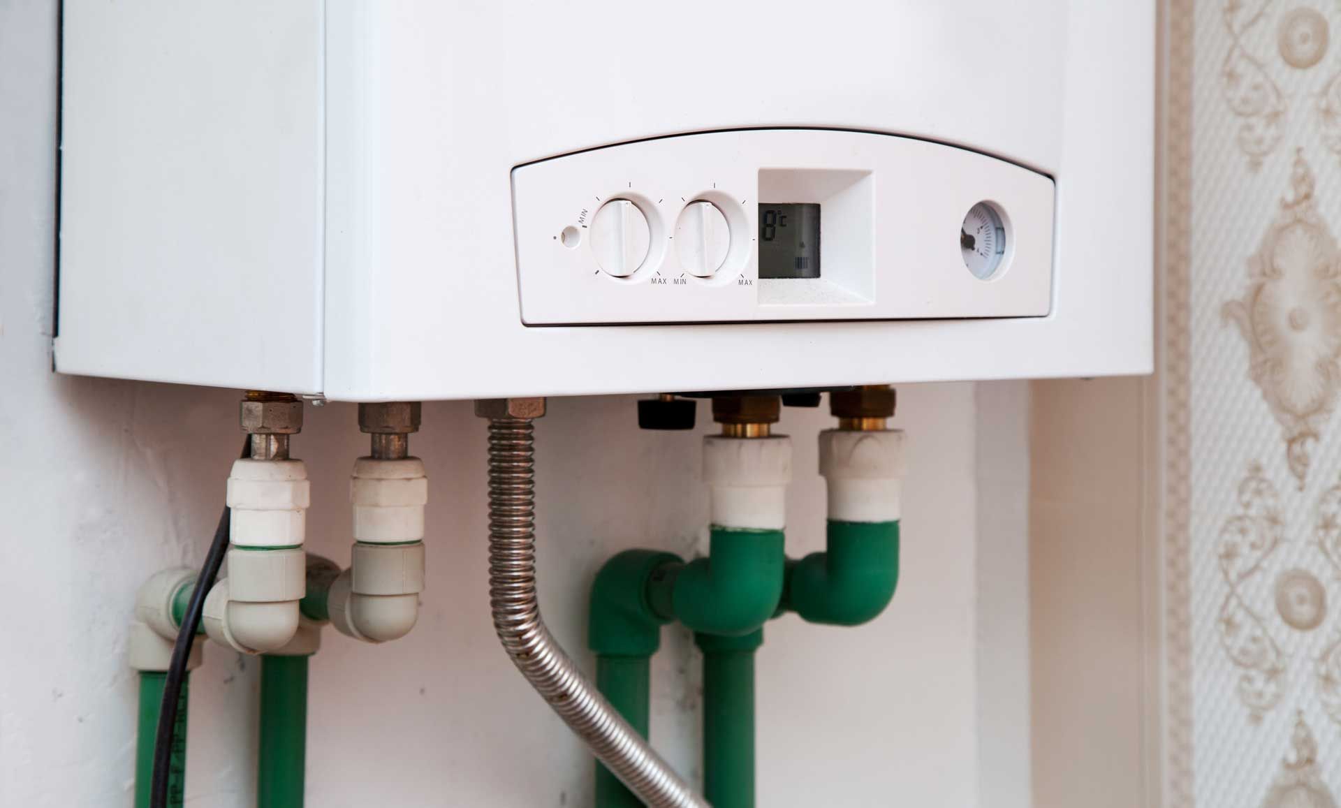 White gas boiler on a wall, with green and white pipes, silver tubing.