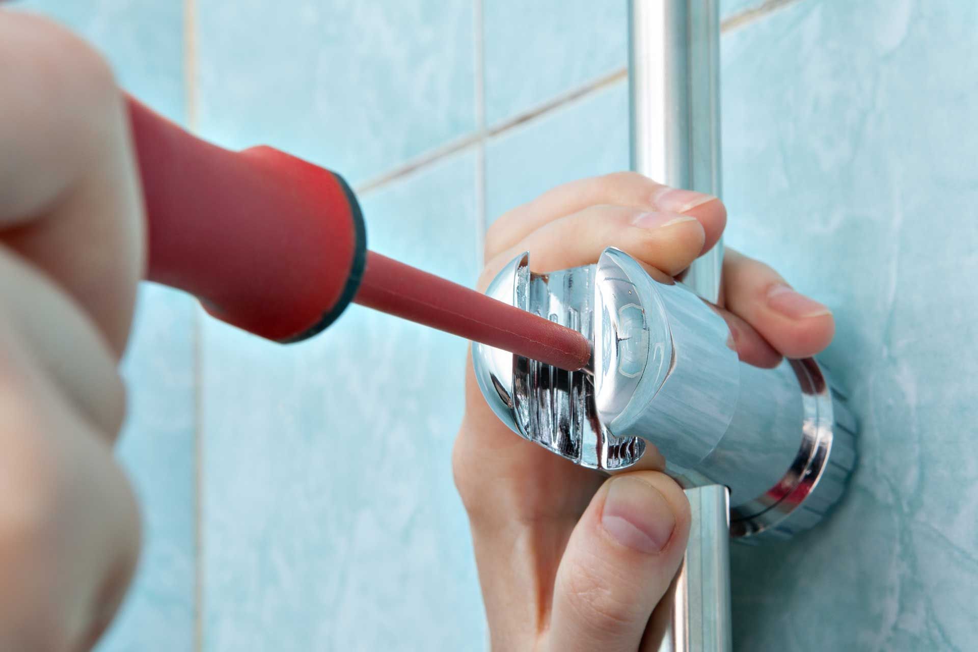 Person using a red screwdriver to secure a chrome shower fixture against a light blue tiled wall.