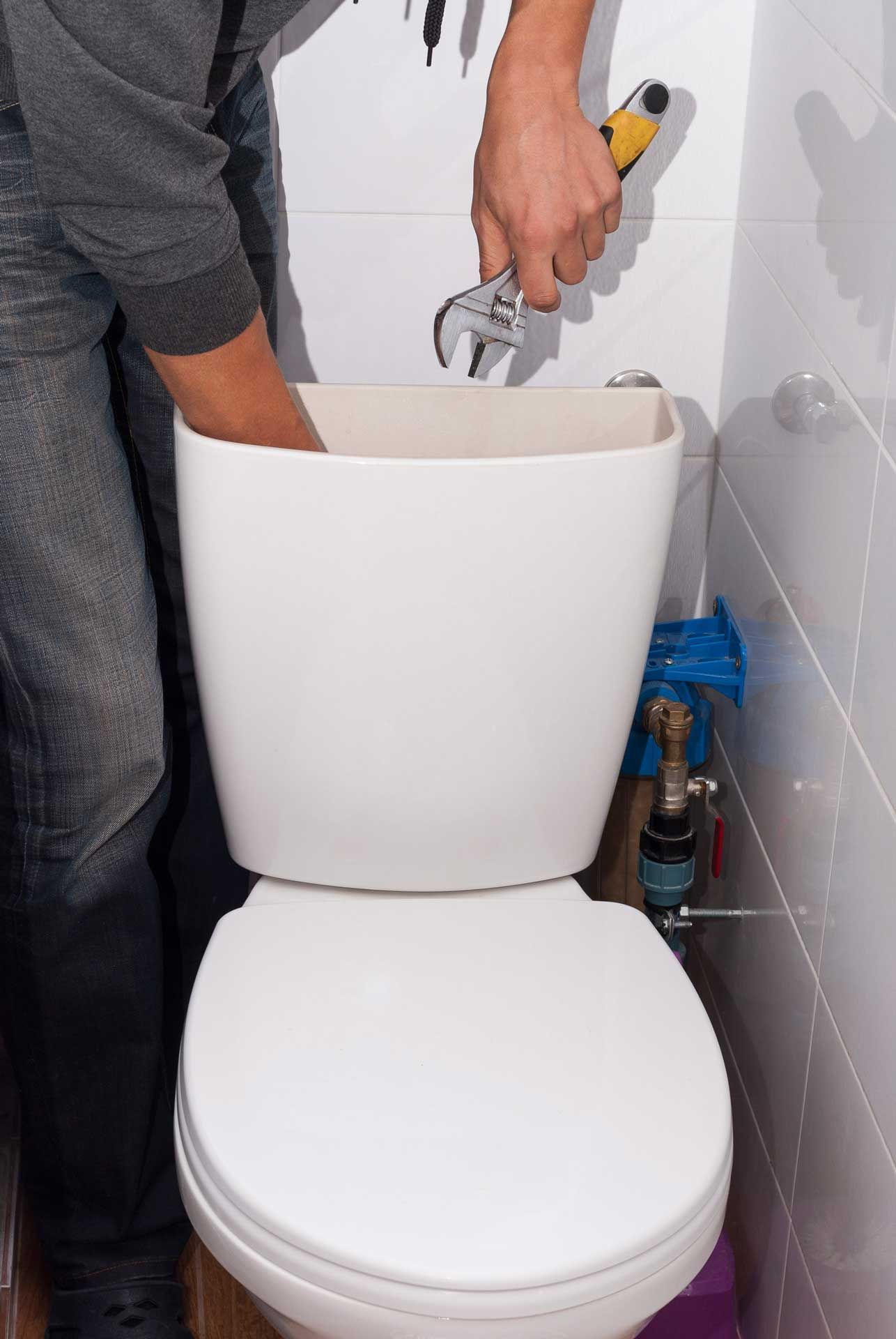 Person repairing a white toilet tank with a wrench in a bathroom.