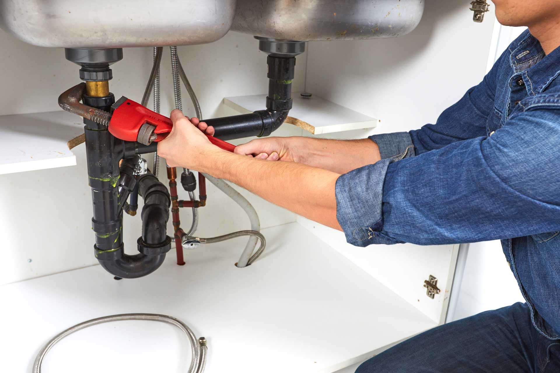Person using a wrench under a kitchen sink to fix plumbing.