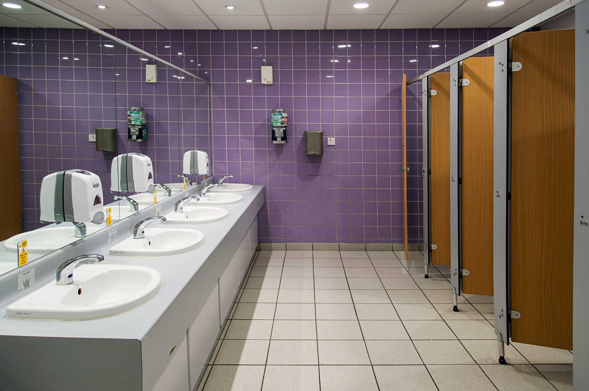 Public restroom with purple tiled walls, white sinks, and wooden stalls.
