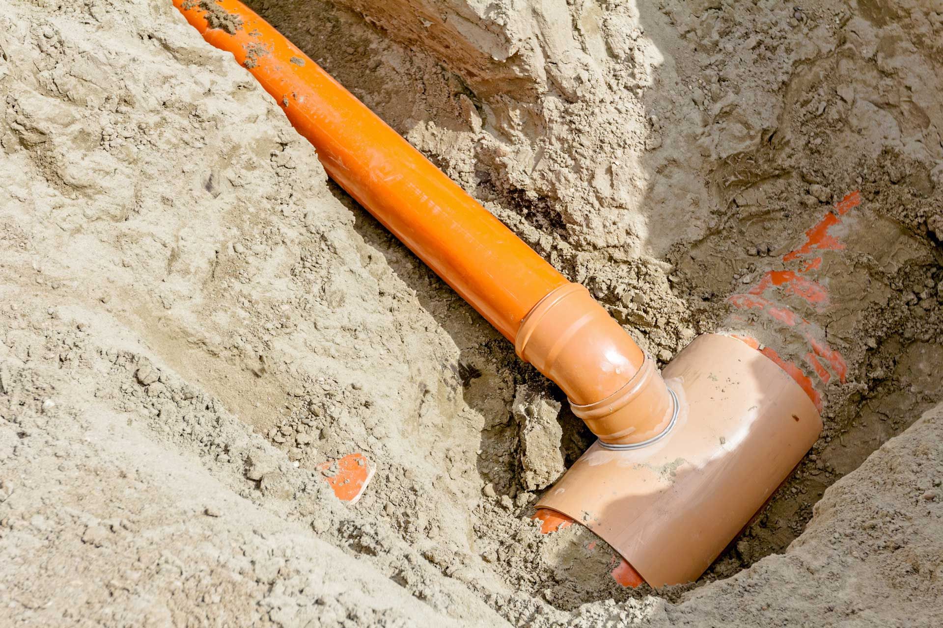 Orange PVC pipes and connectors installed in a sandy trench.