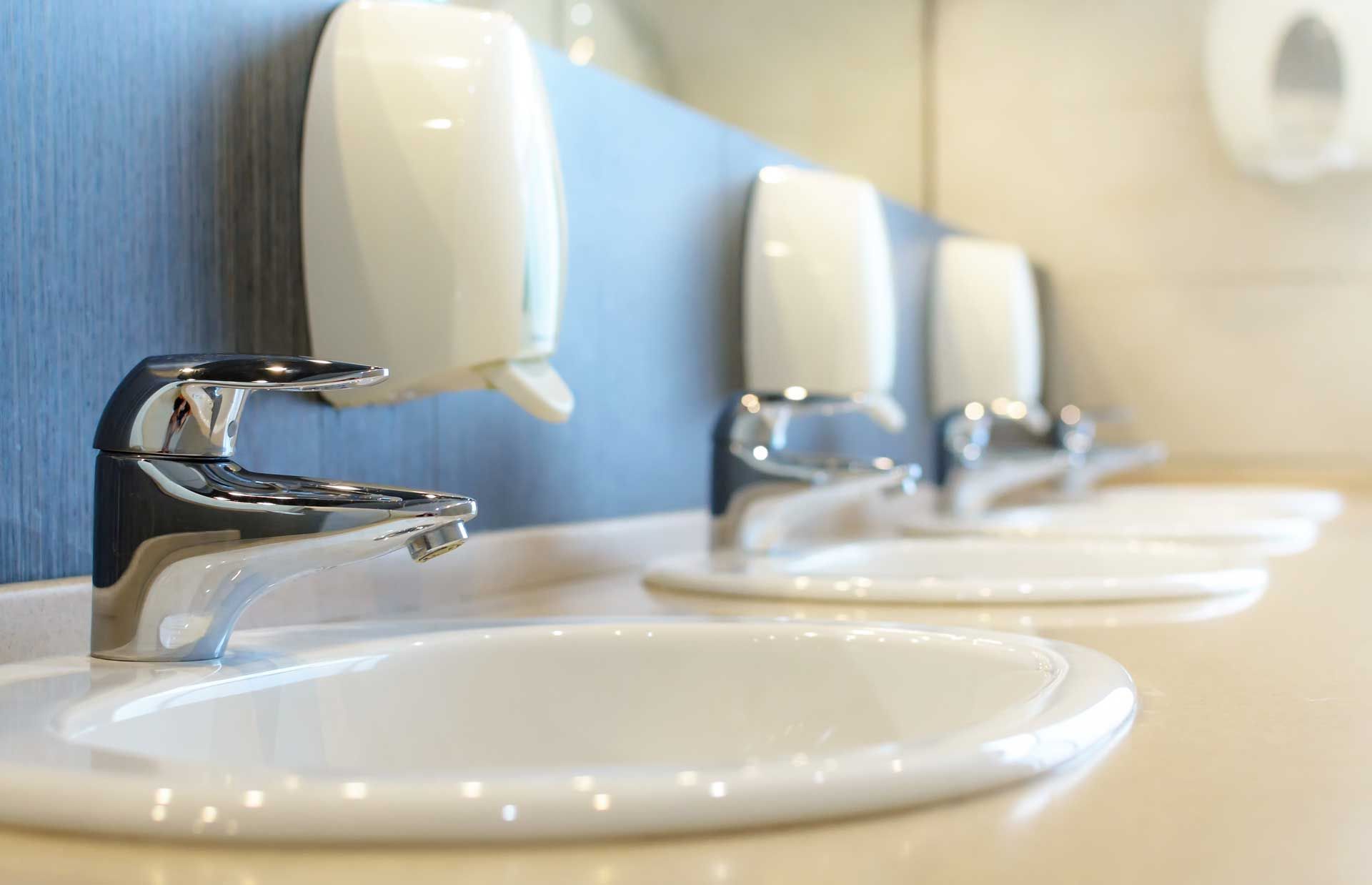 Row of white sinks with chrome faucets and soap dispensers in a public restroom.