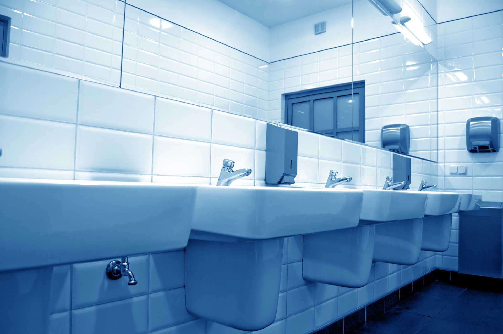 Public restroom with white sinks, tile, and mirror, in a cool blue tone.