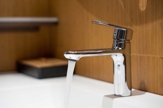 Chrome faucet pouring water into a white sink, set against a wooden wall.