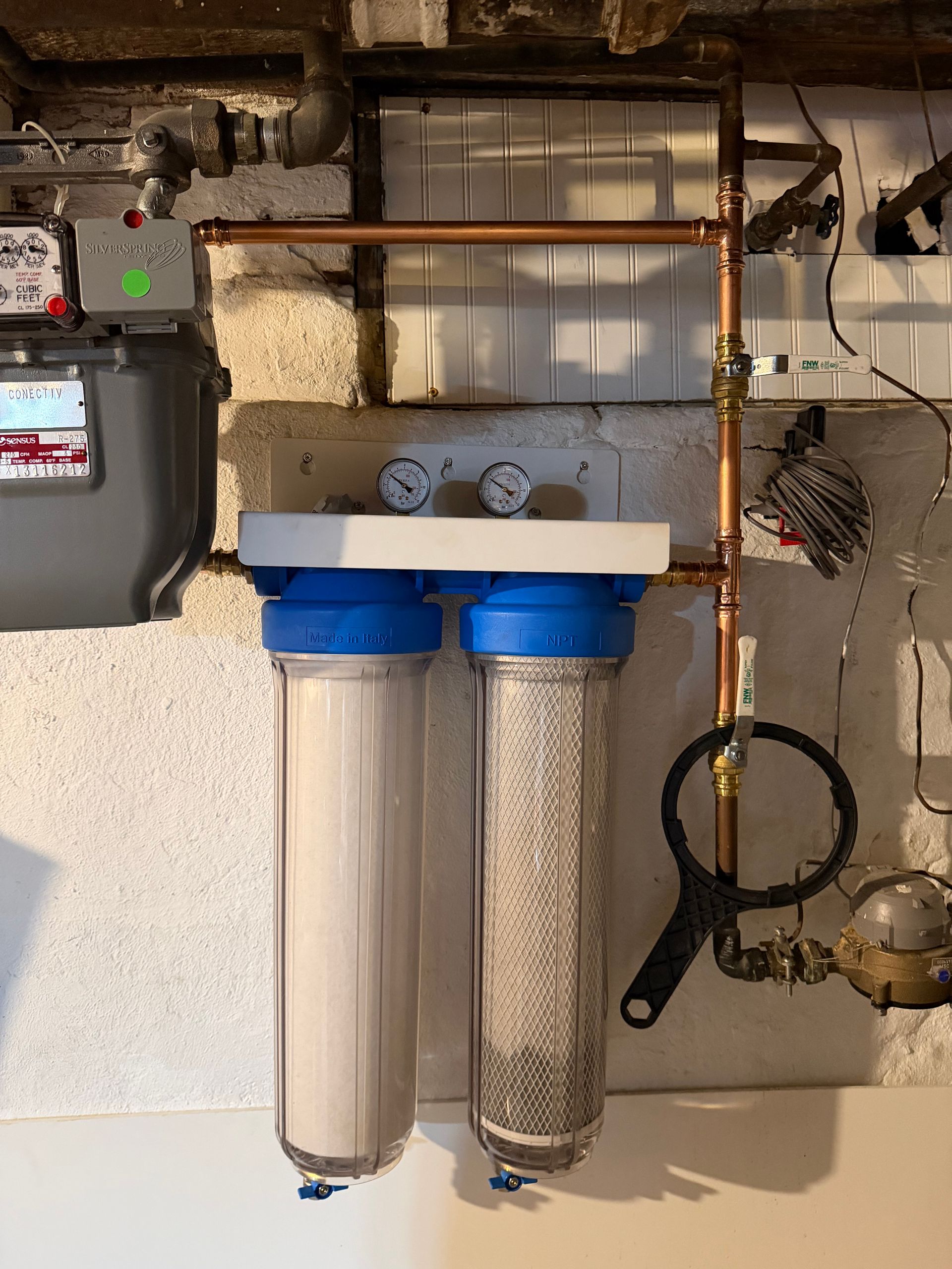 A shiny kitchen faucet over a double sink, with soap dispenser and light switches visible.