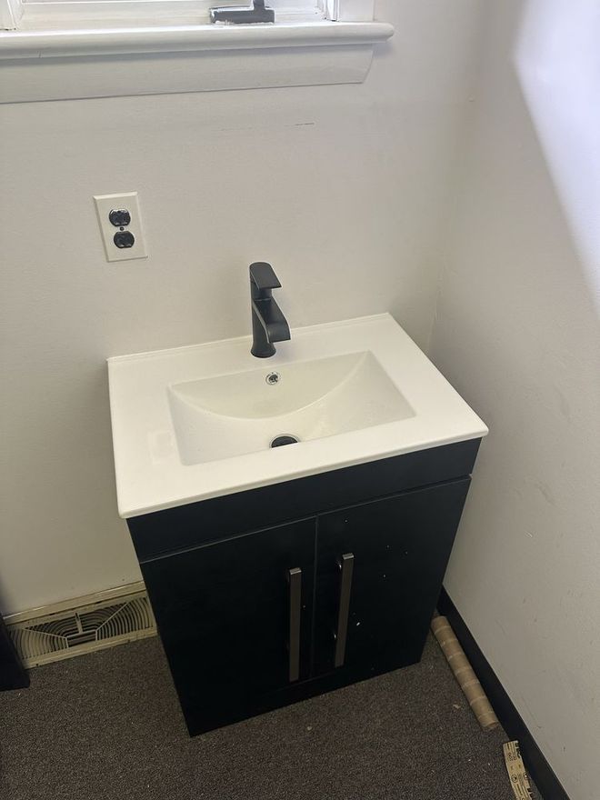 Black bathroom vanity with white countertop and black faucet against a white wall. Black bathroom vanity with white countertop and black faucet against a white wall.