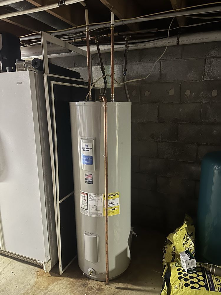 A tall, cylindrical water heater with copper pipes in a basement next to a refrigerator.
