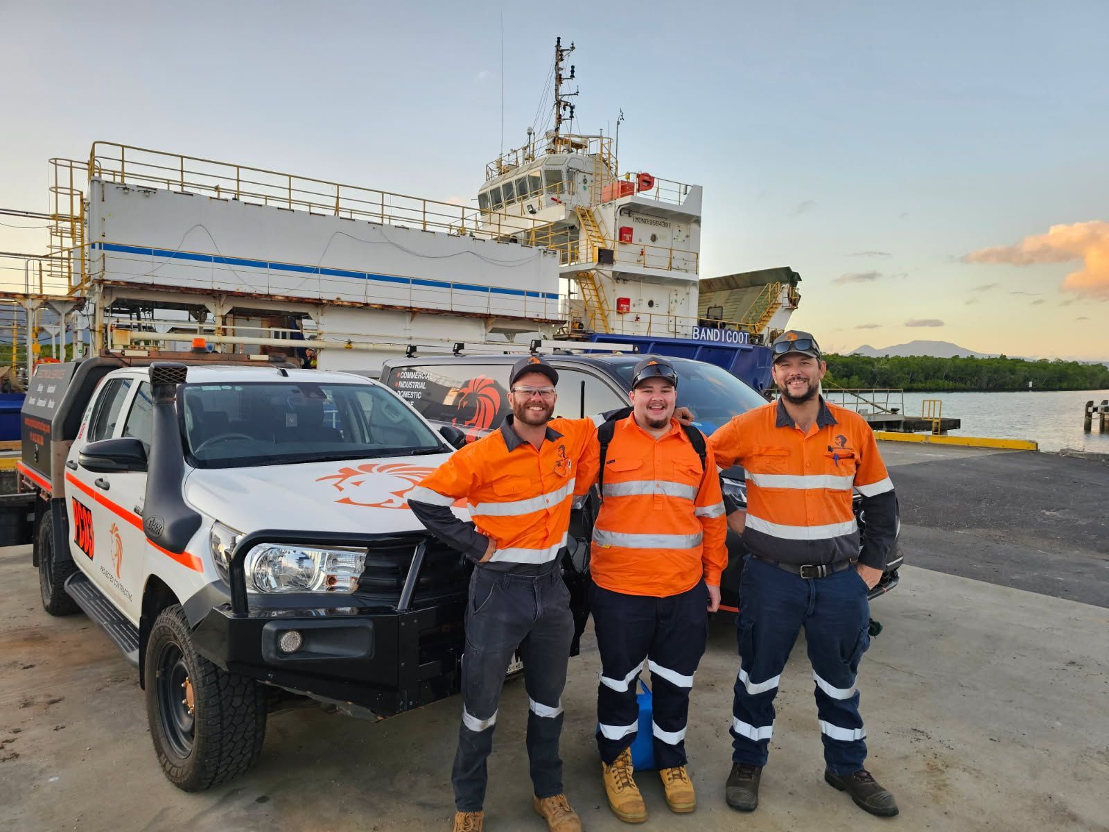 Three male workers in orange hi-vis shirt standing in front of work car at a boat ramp — Projected Contracting Electrical Services In Portsmith, QLD