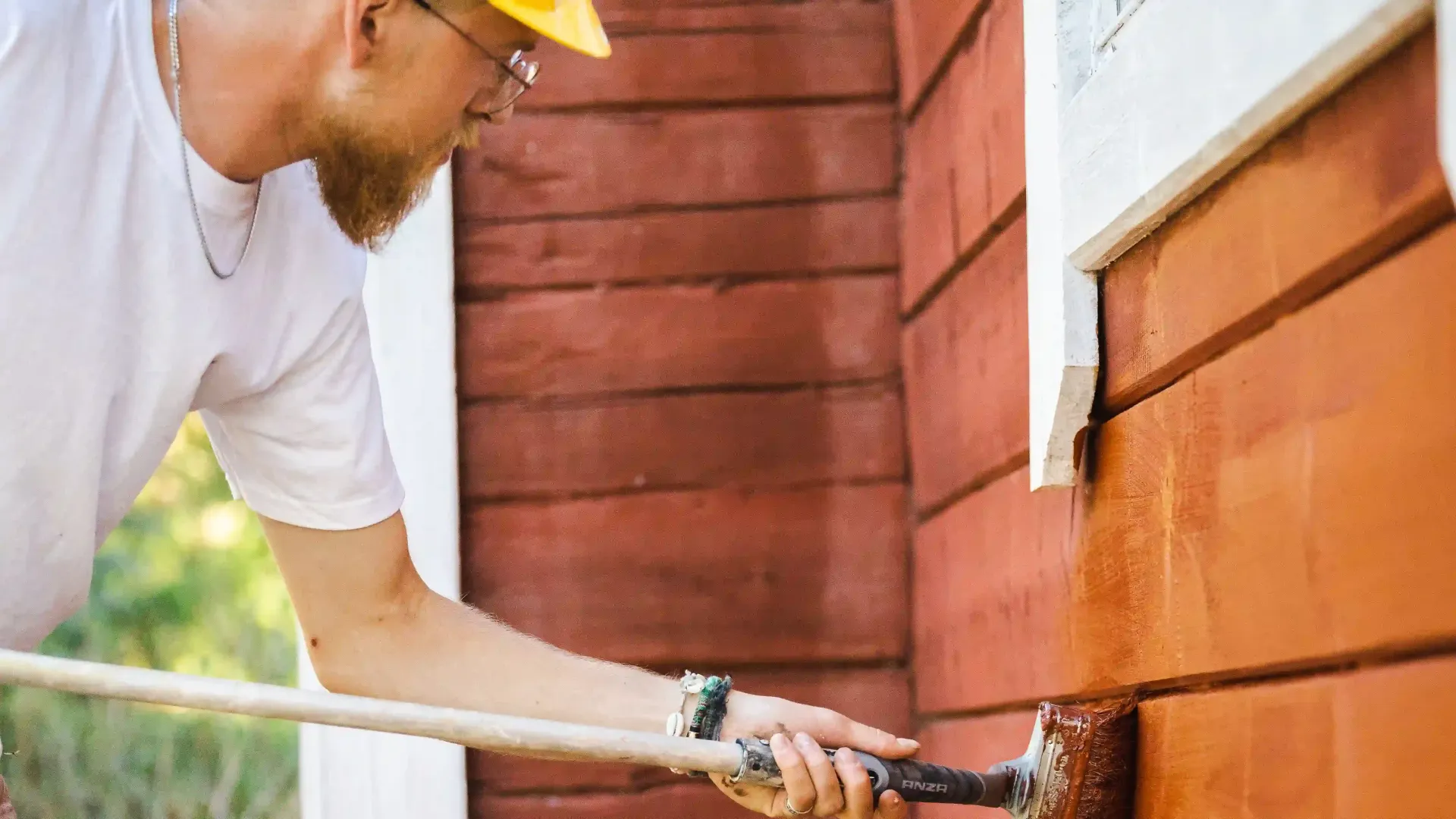 Maalari tekee pintamaalausta puutalon seinään