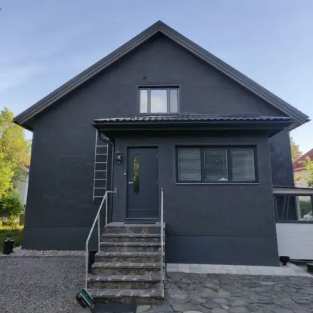 Maalausmestari maalaa tumman omakotitalon ulkoverhousta.