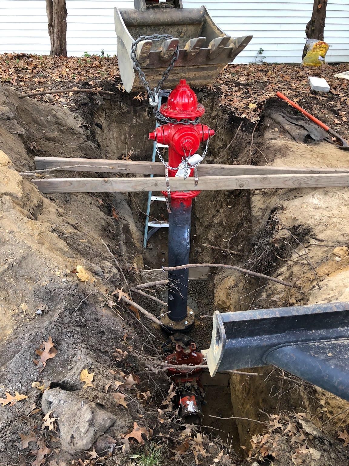 Red fire hydrant in a muddy trench with exposed pipes and wooden braces outdoors