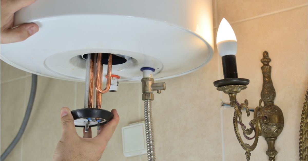 Hand tightening a bathroom sink drain under a white basin beside a lit wall sconce