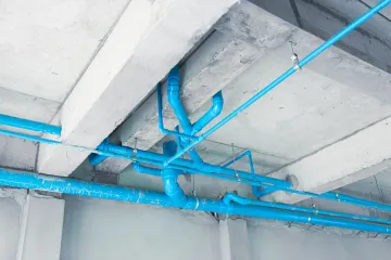 Blue pipes and conduits running across a concrete ceiling in an unfinished building interior