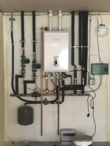 Wall-mounted boiler and heating pipes in a utility room, with gauges, valves, and a small control box.
