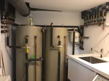 Boiler room with two large tanks, pipes, valves, and a sink in a utility space