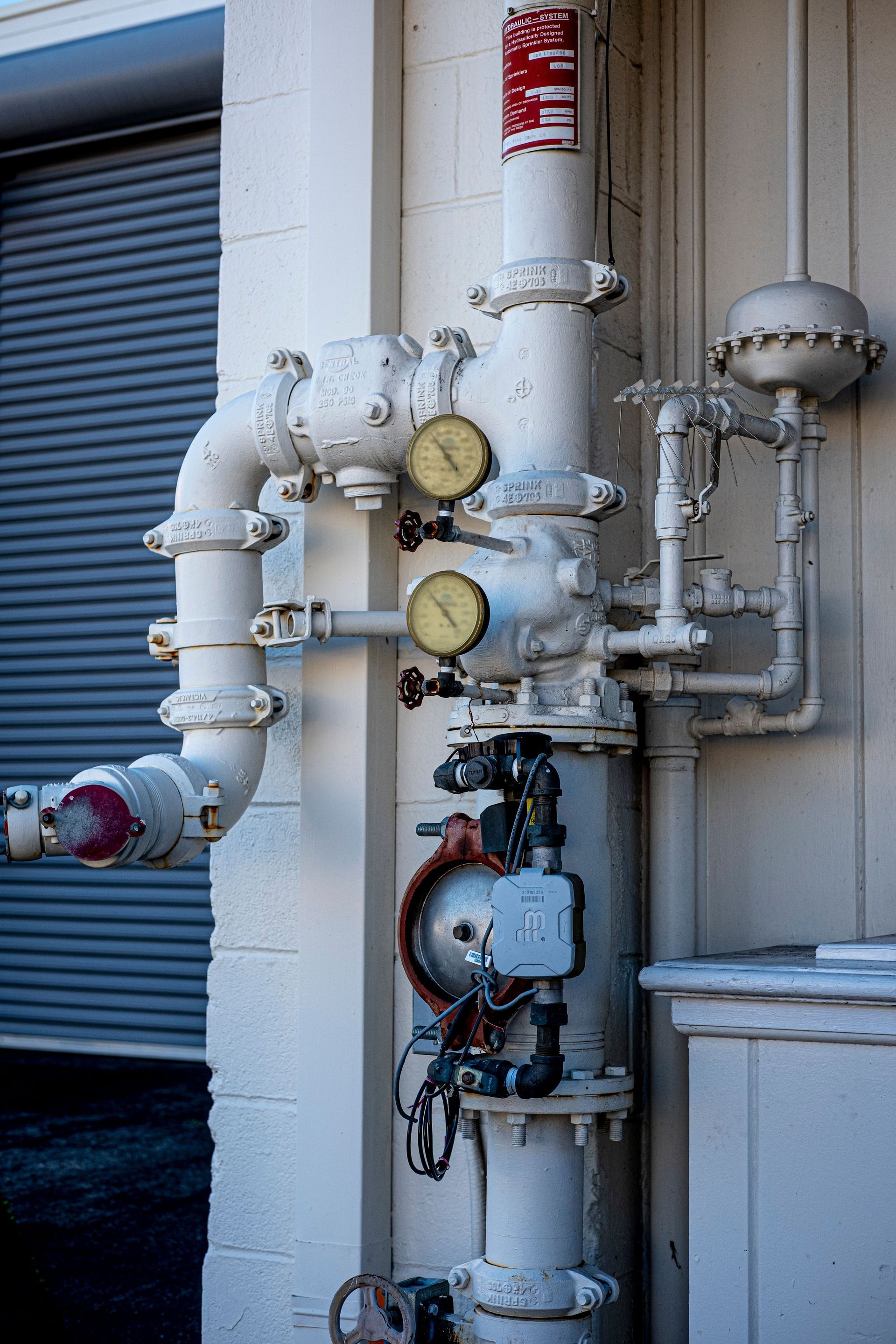 Industrial pipe assembly with gauges and valves mounted on an exterior wall