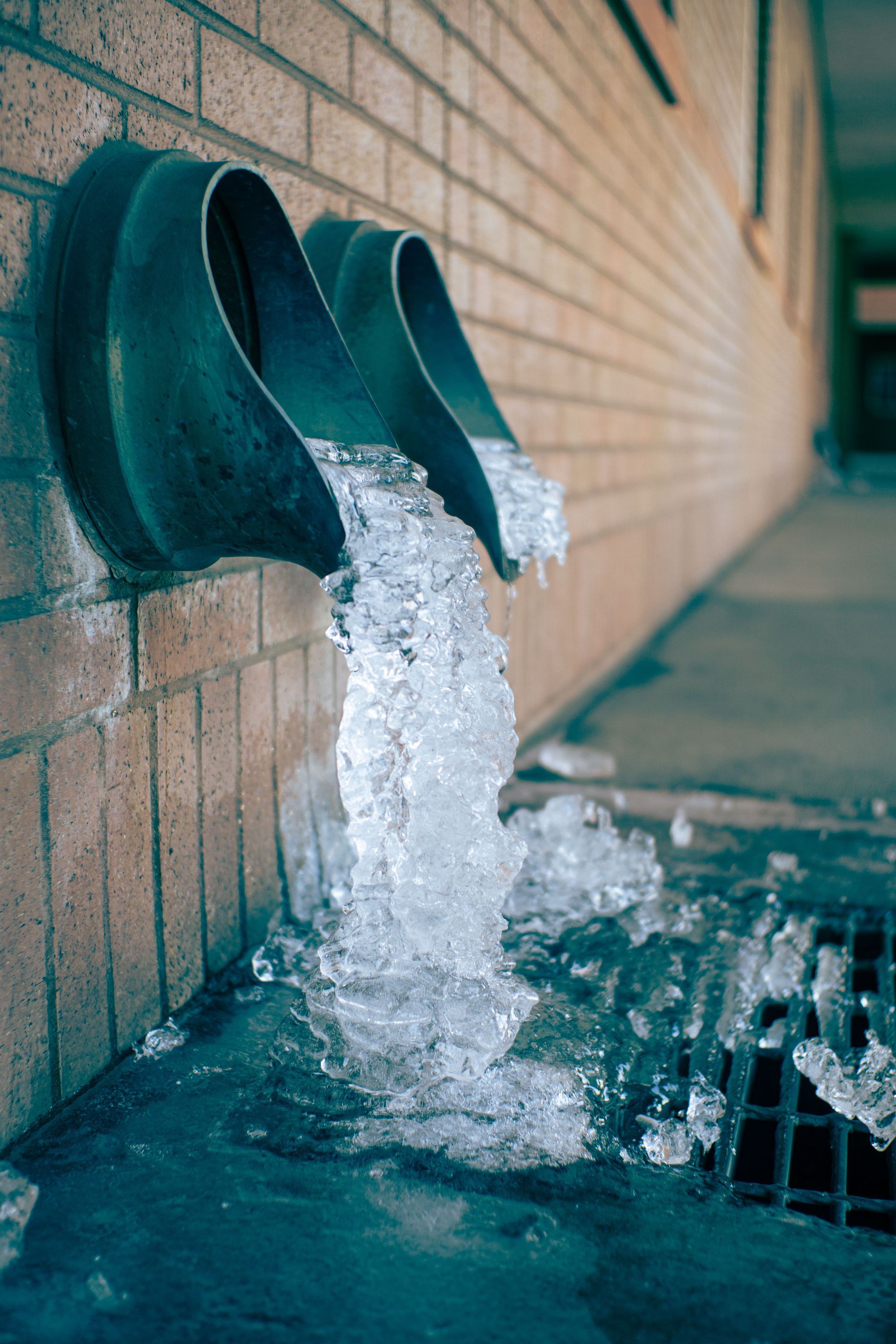 Frozen water pouring from pipes along a brick wall into a basin