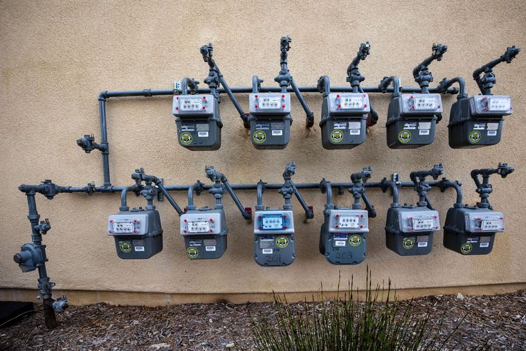 Two rows of gas meters mounted on a beige exterior wall.