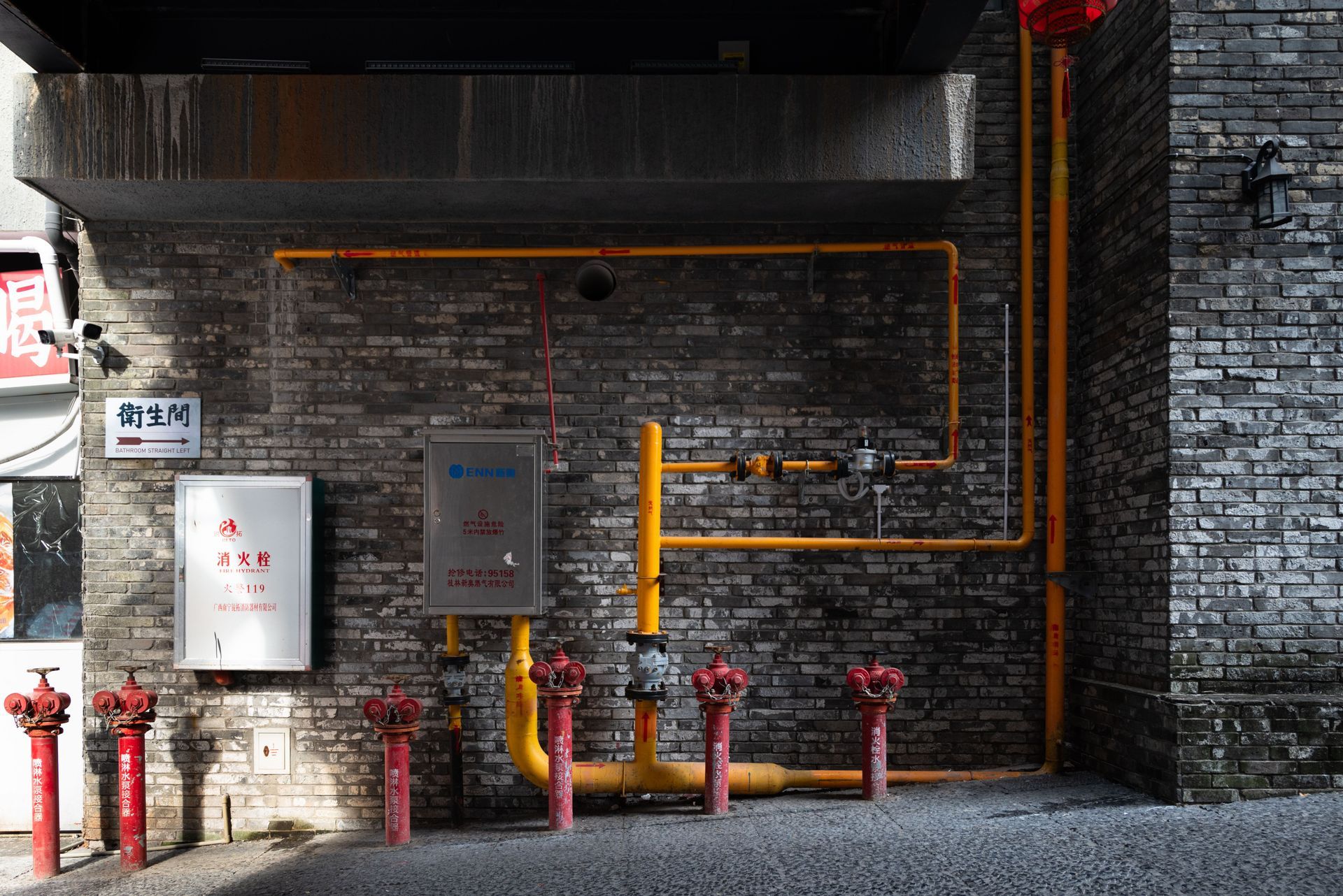 Gray brick wall with orange pipes and red fire hydrants in an industrial alley.