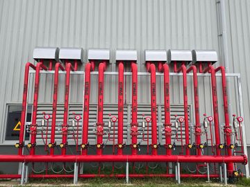 Row of red industrial pipes and valves mounted against a corrugated metal wall