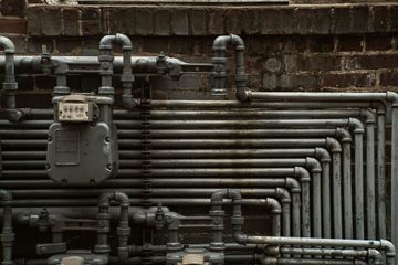 Gray gas pipes and meters mounted on a brick wall, forming a dense industrial pattern.