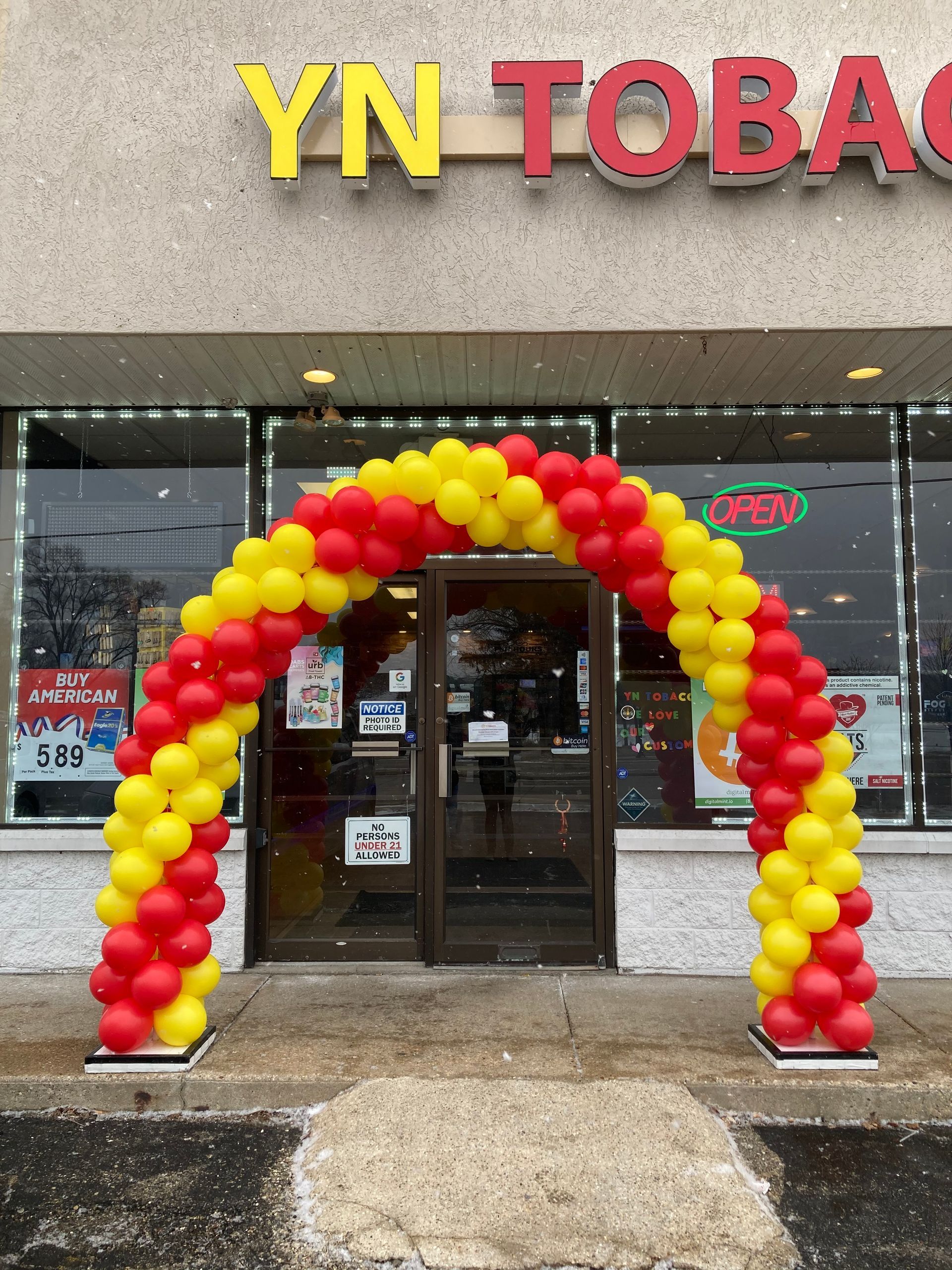 A red and yellow balloon arch is in front of a store called yn tobacco