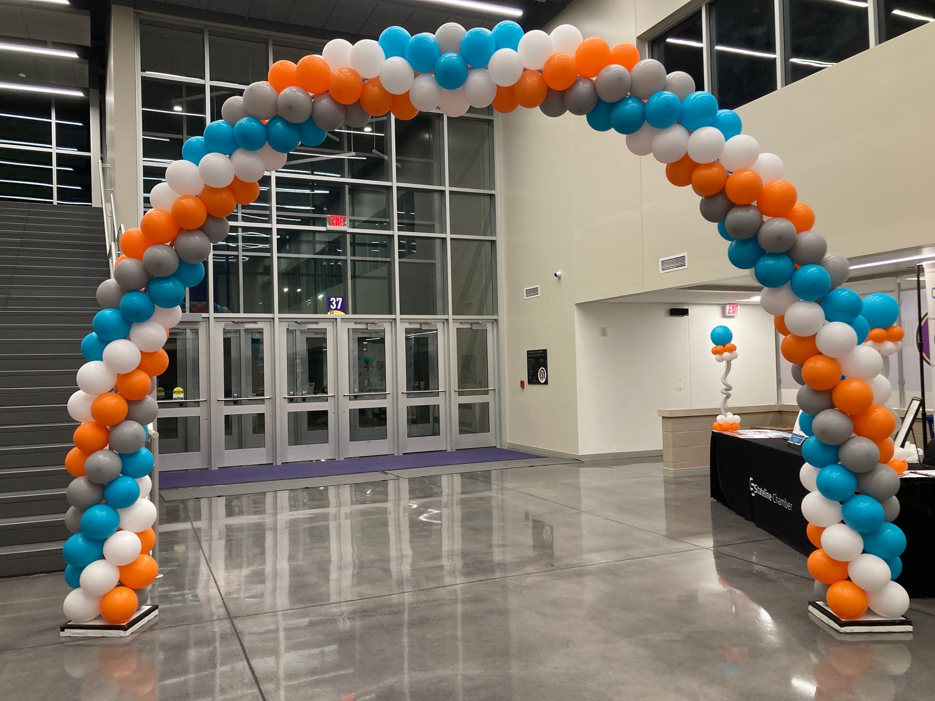 A large arch made of orange , white , and blue balloons in a hallway.