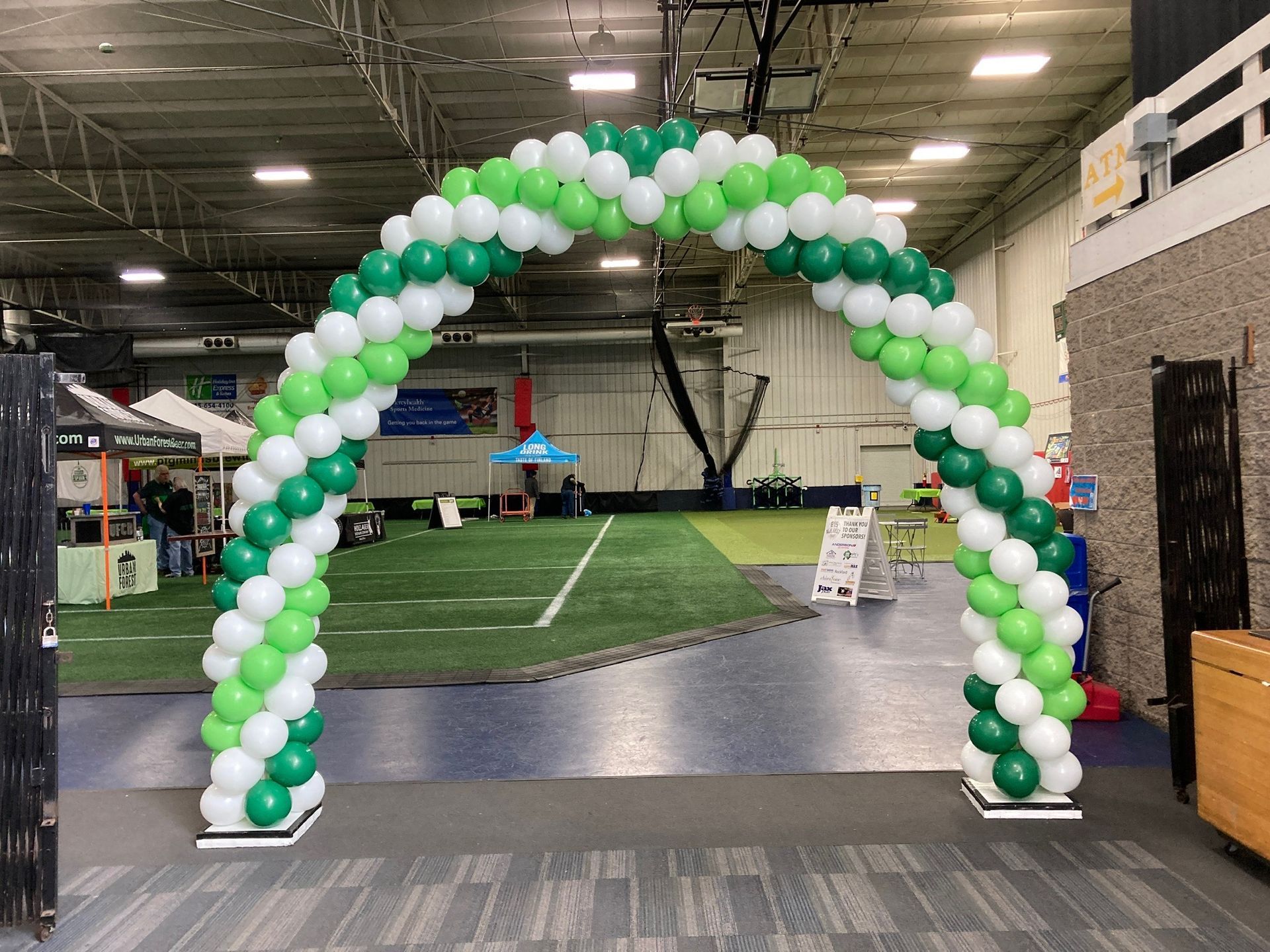 A green and white balloon arch in a gym.
