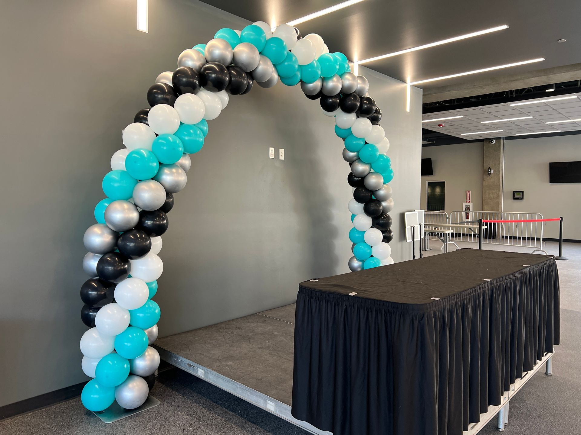 A table with a black skirt and a balloon arch in a room.