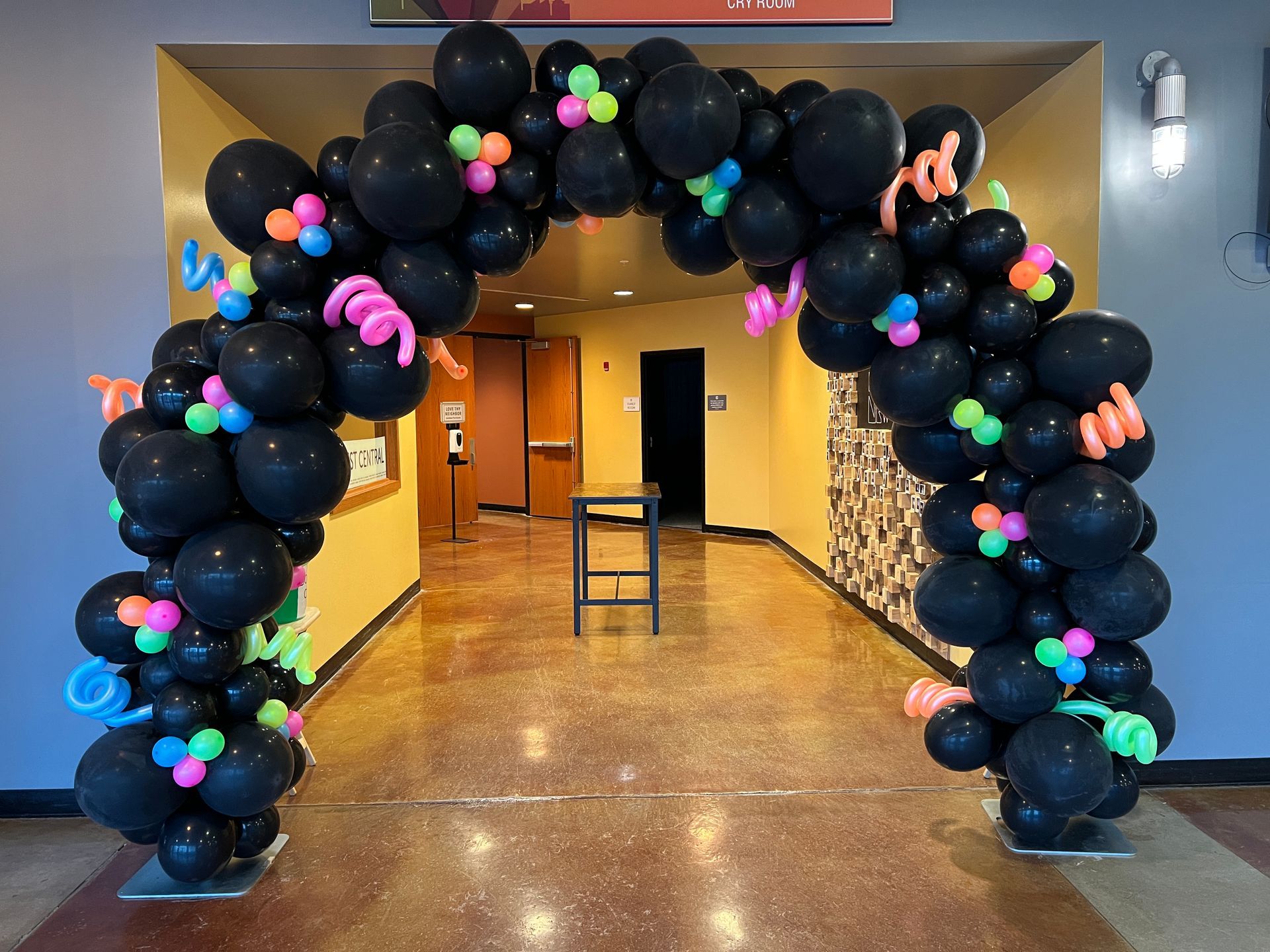 A hallway is decorated with black balloons and neon balloons.