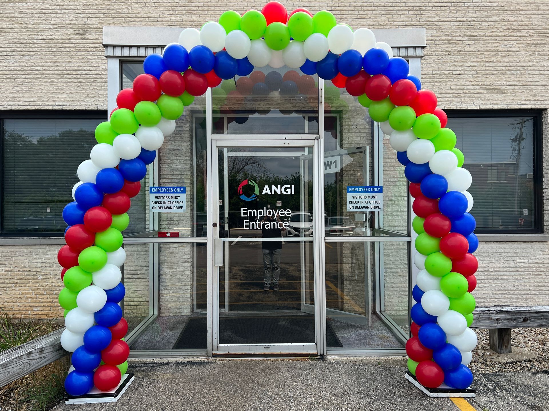 A red , white , and blue balloon arch is in front of a building.