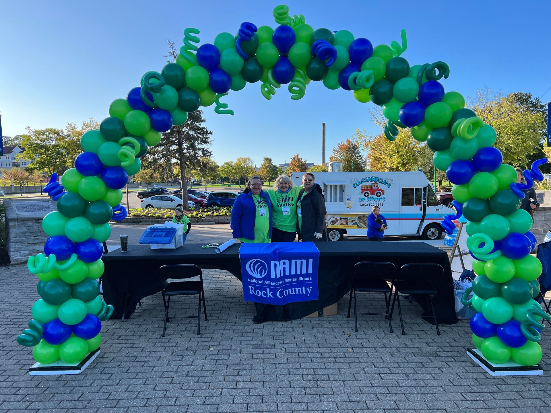 A green and blue balloon arch is surrounding a table and chairs.