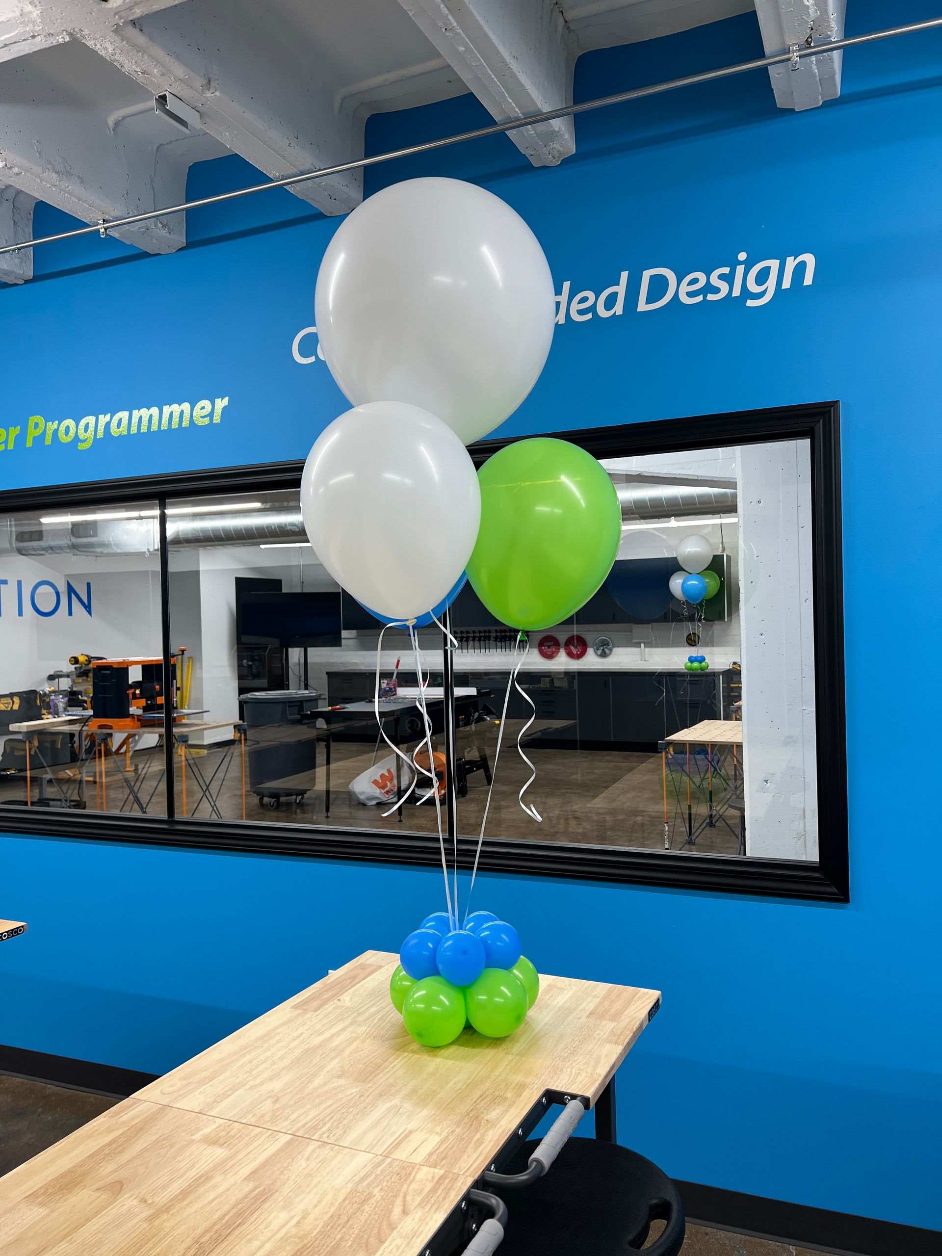 Three balloons are sitting on a table in front of a blue wall that says created design