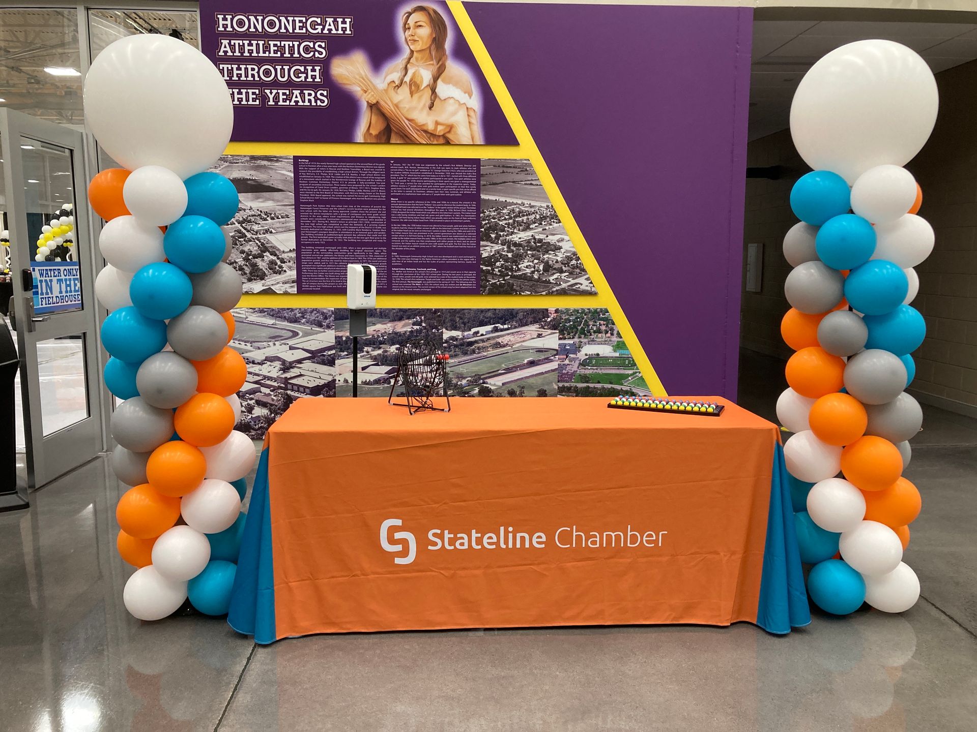 A table with an orange tablecloth is surrounded by balloons.