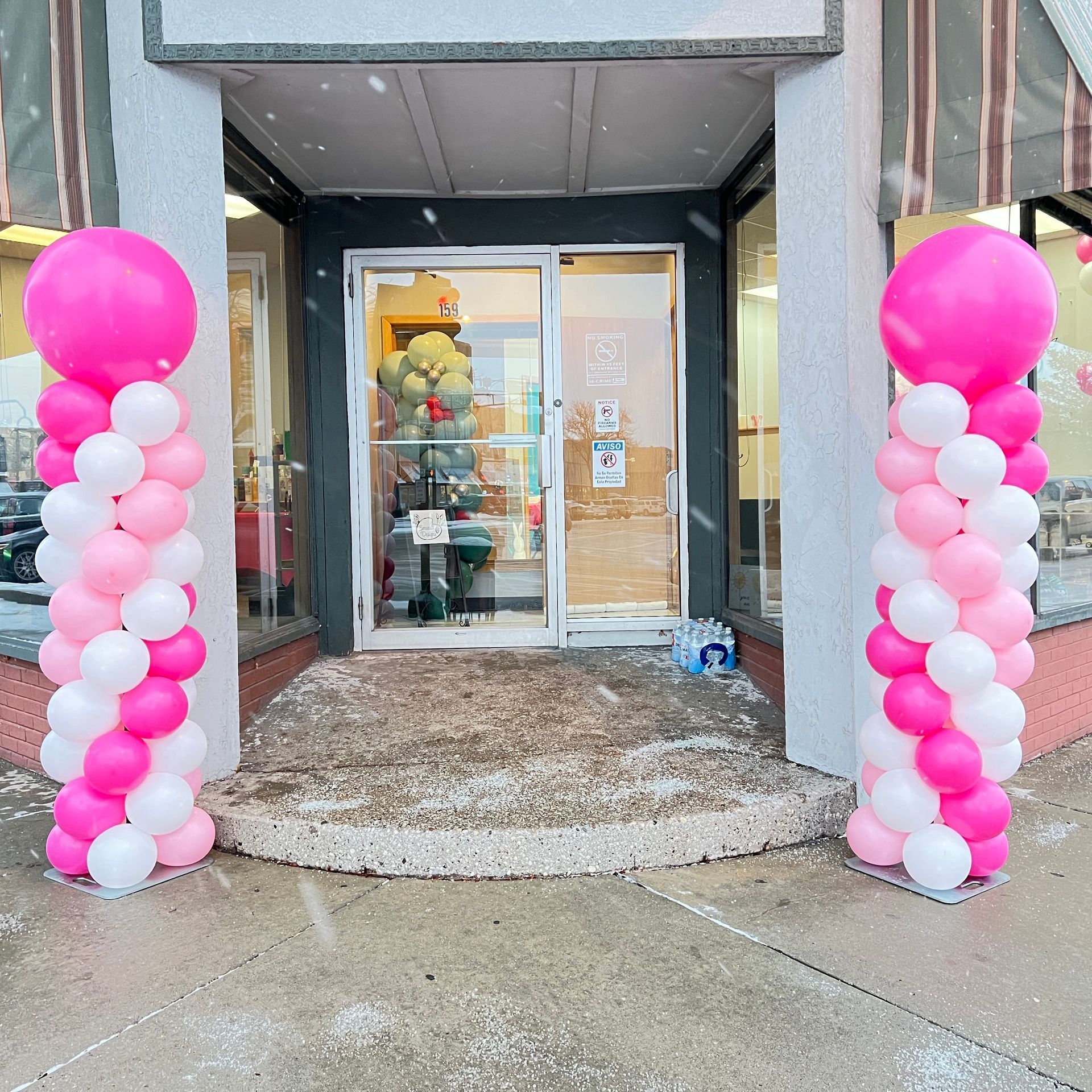 Pink and white balloons are lined up in front of a store