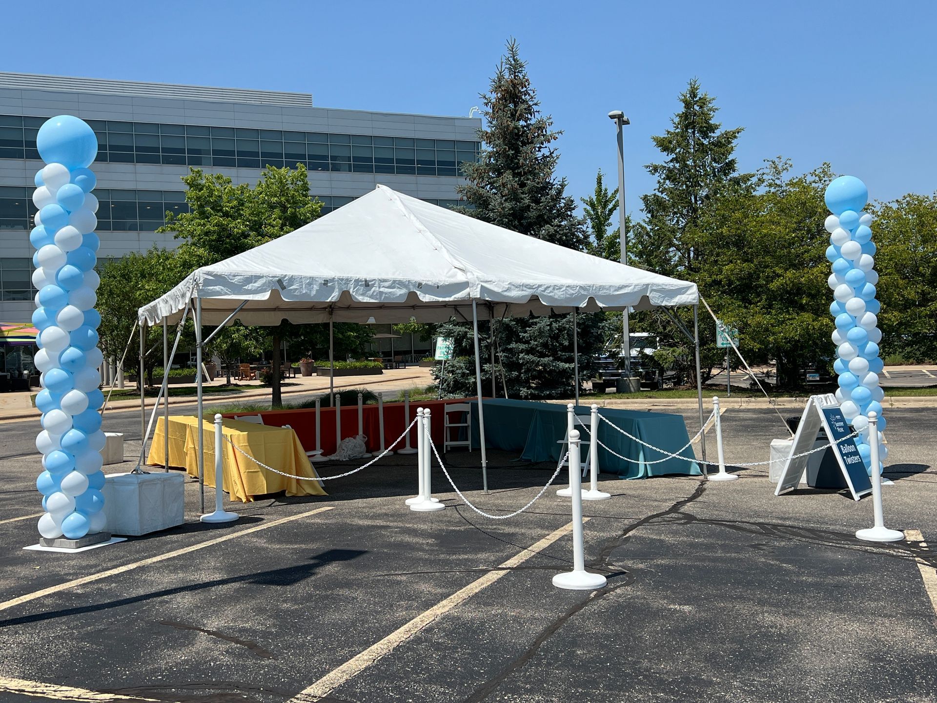 A white tent with blue and white balloons in a parking lot