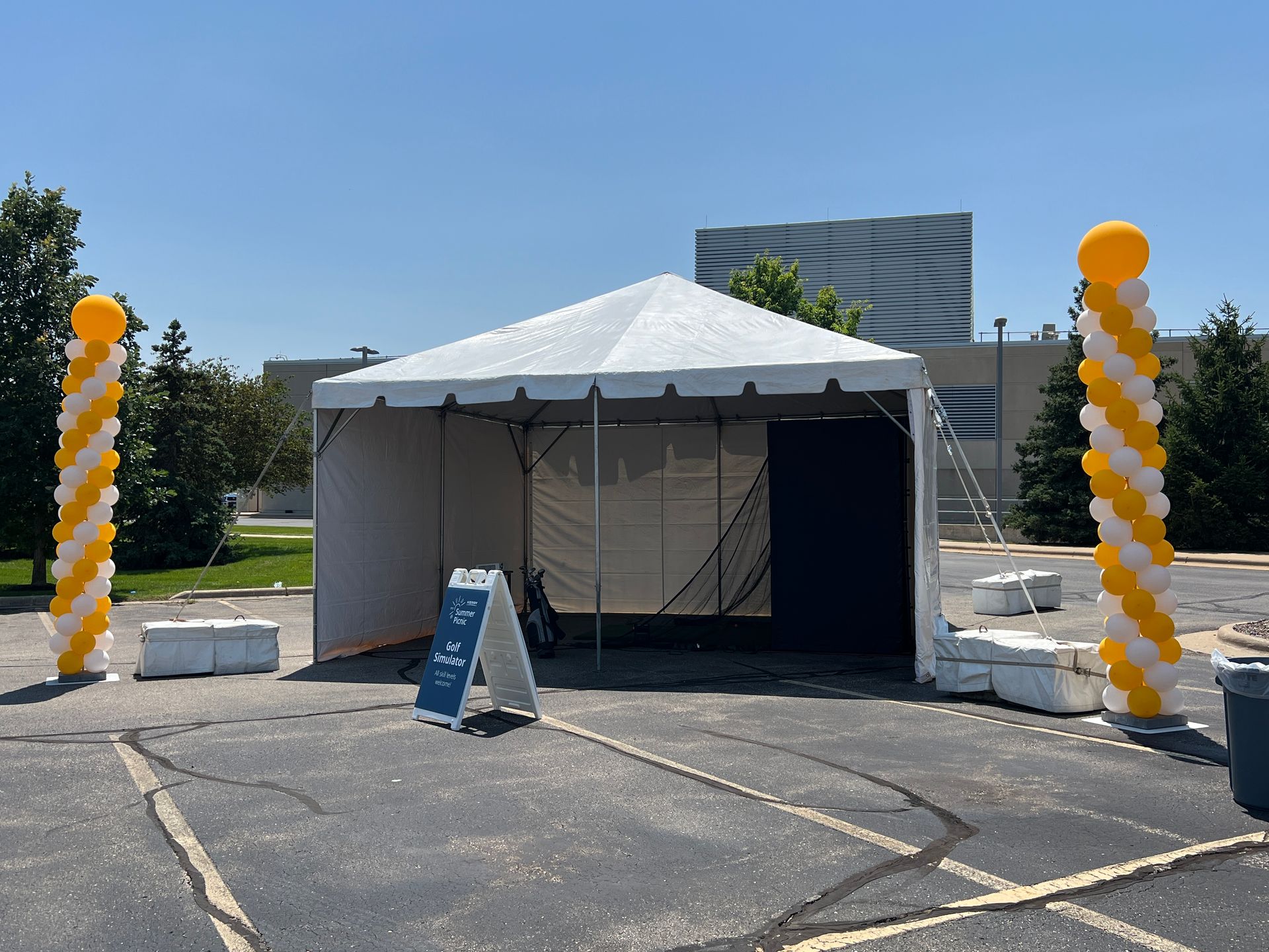 A white tent with yellow and white balloons in a parking lot.